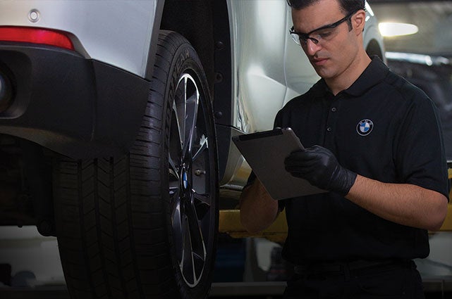 BMW Service Technician in service bay inspecting a BMW on a lift